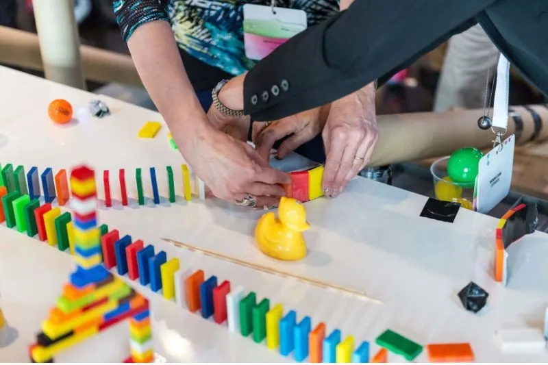 Domino Challenge 2.0: Hände stellen bunte Dominosteine und Bausteine auf einem Tisch auf